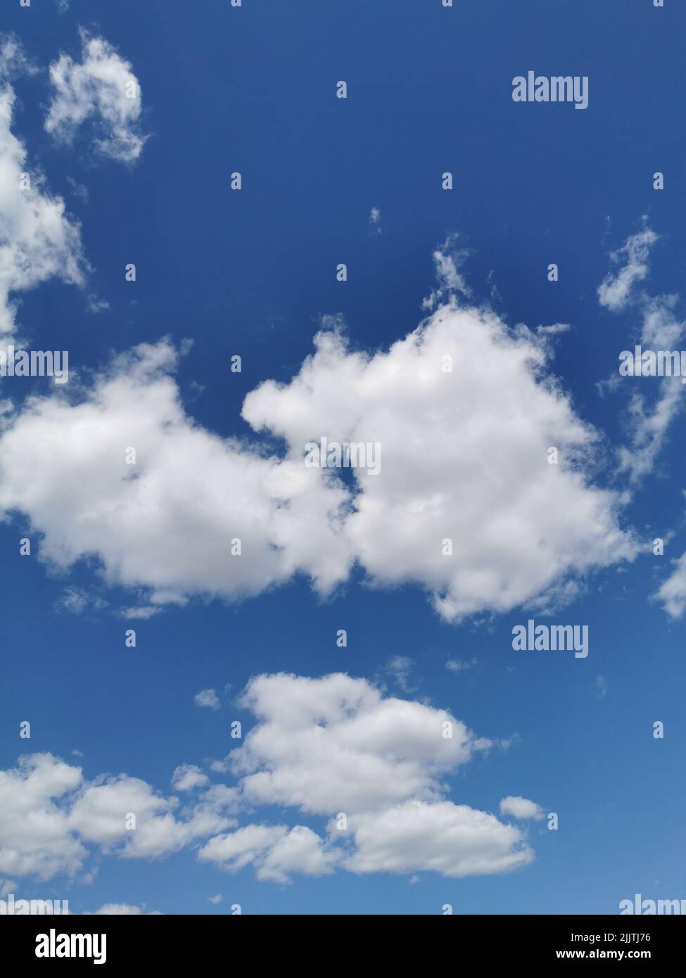 A vertical shot of cotton-like white clouds in the endless blue sky Stock Photo