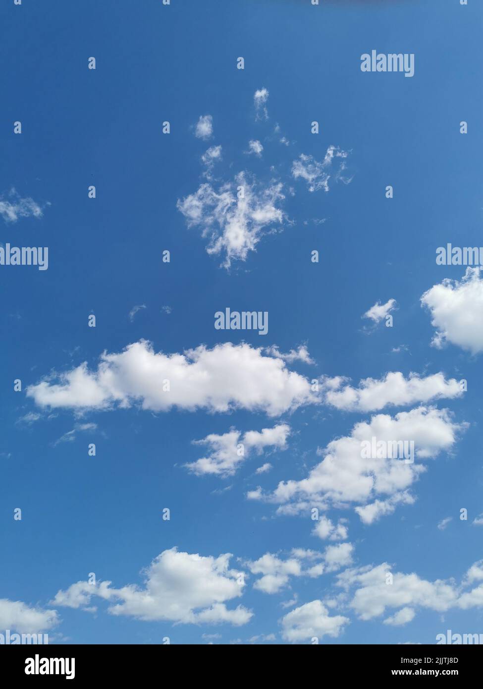 A vertical shot of white fluffy clouds hovering in the blue sky Stock Photo