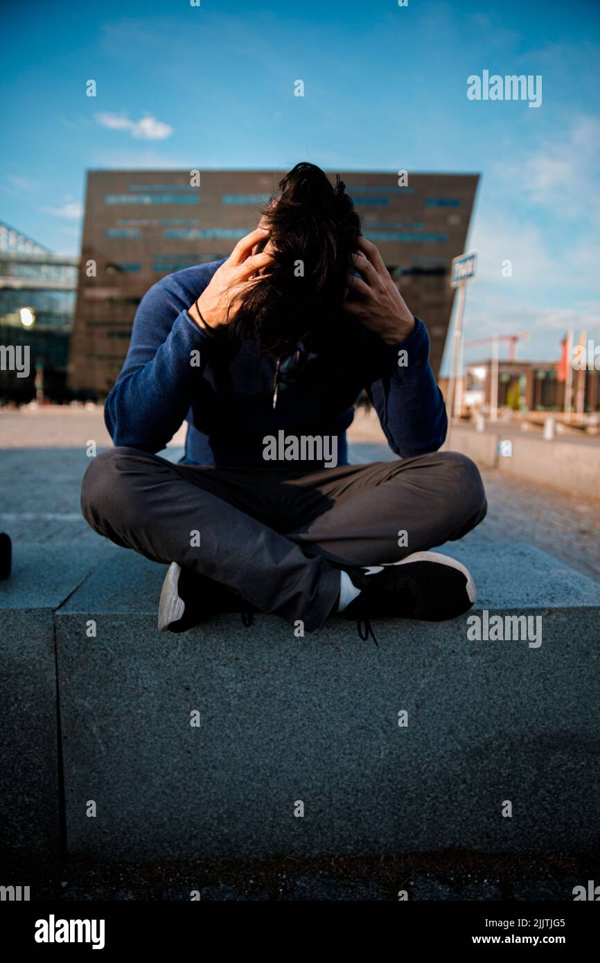 A man sitting alone in the street and looking upset or with a pain in the head Stock Photo