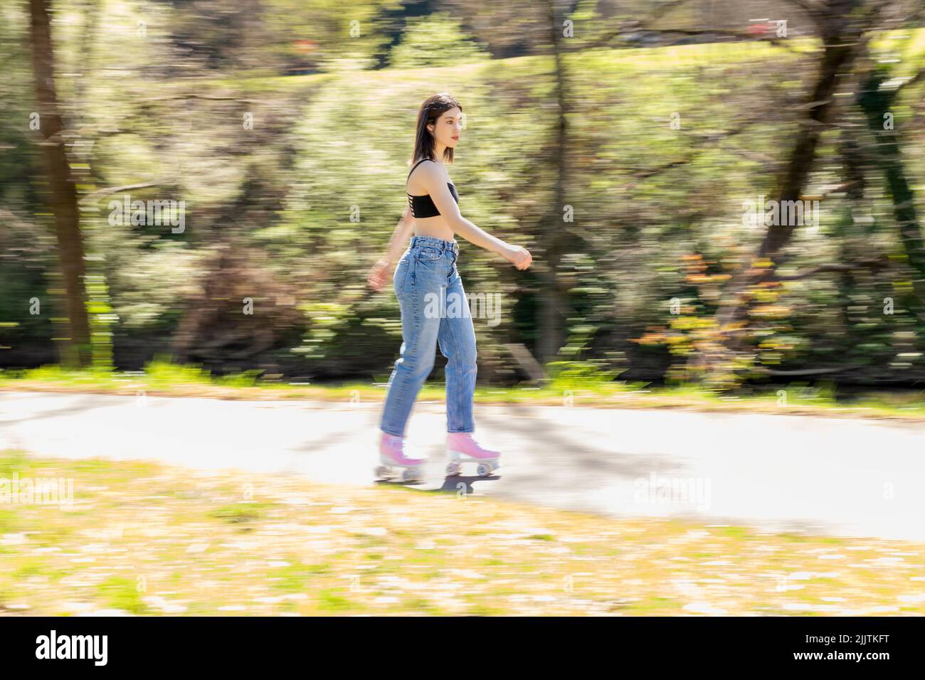 brunette woman skating in a park with pink roller skates Stock Photo