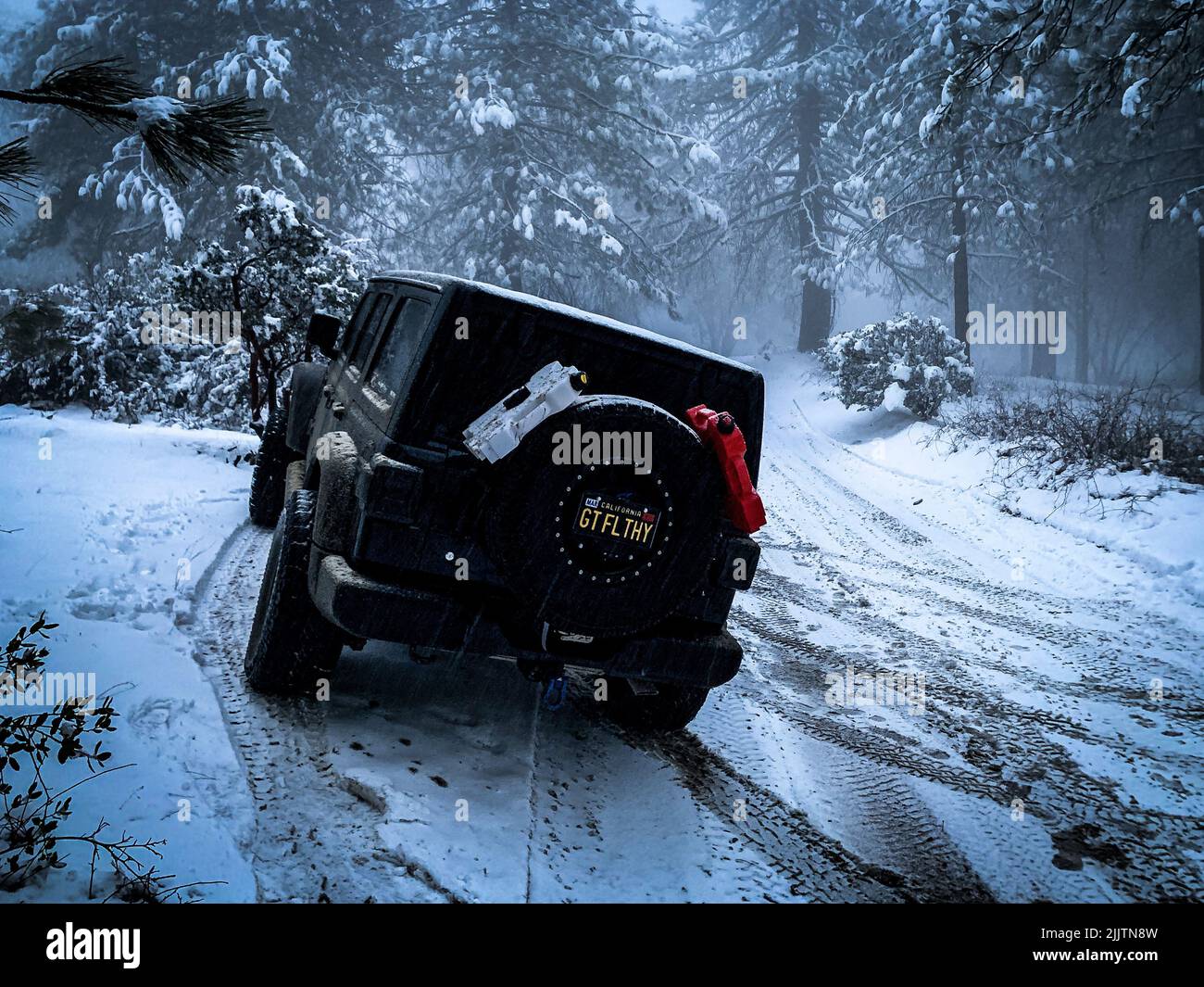 A back view of a black Jeep Wrangler off-roading on the snow-covered roads of Riverside, US Stock Photo
