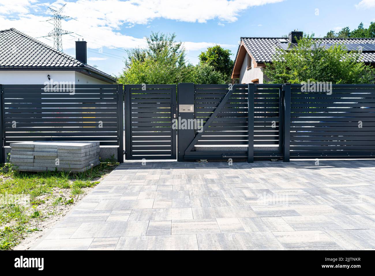A modern panel fence in anthracite color, a visible sliding gate to the garage and a wicket with a letterbox. Stock Photo