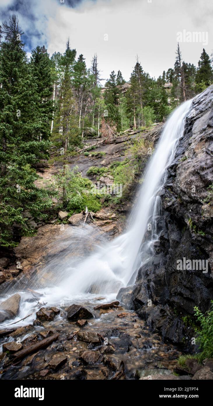 A vertical shot of a waterfall flowing from a rocky cliff in a forest ...