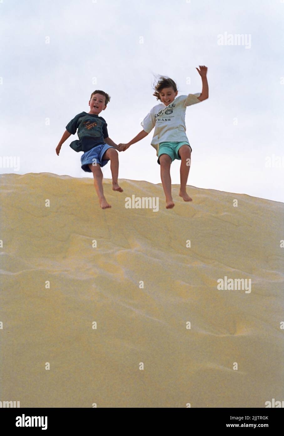 Children - brother and sister - having great fun jumping down a sanddune, Mungo Brush, Myall Lakes, New South Wales, Australia Stock Photo