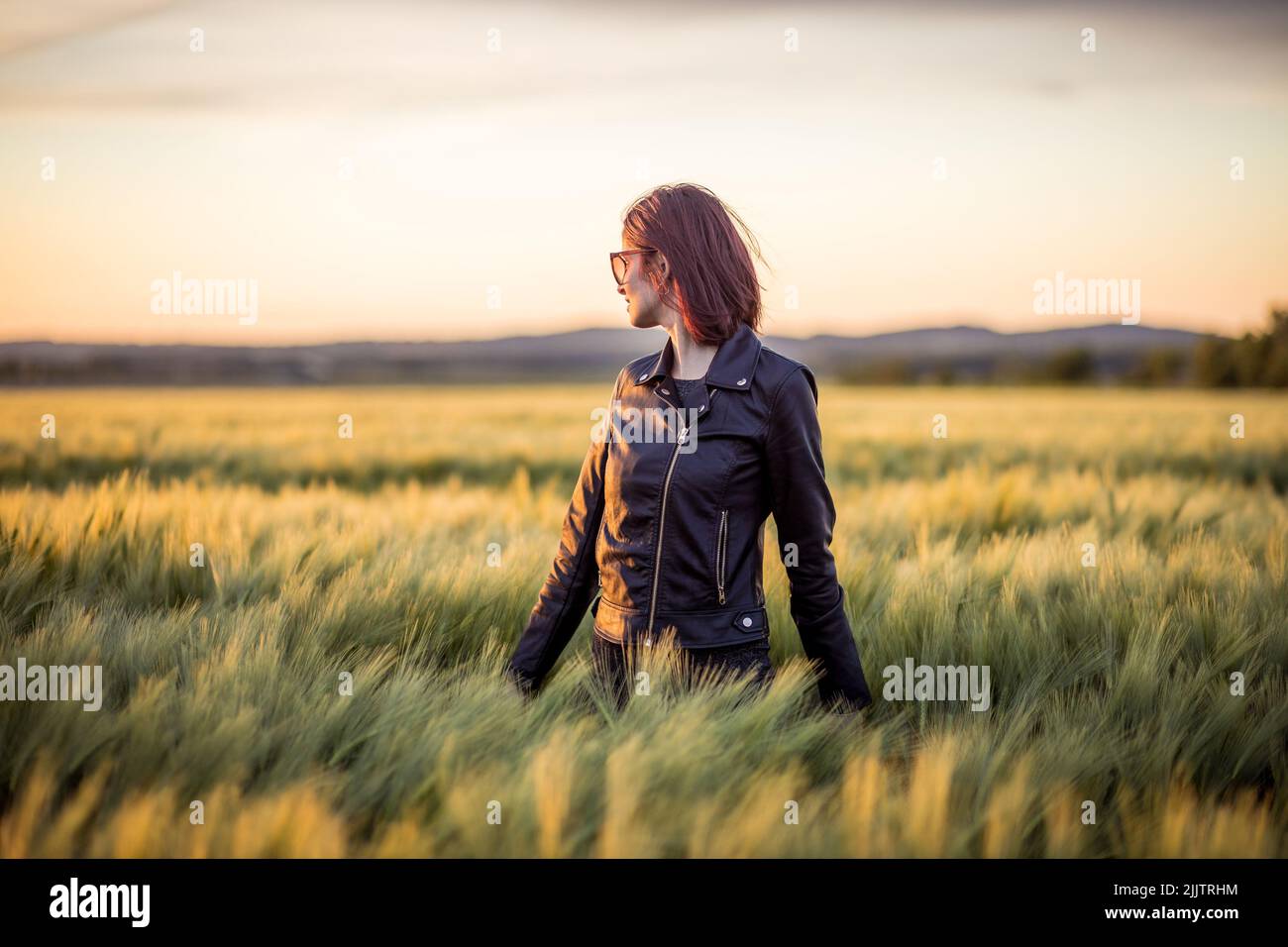 A beautiful portrait of a young girl standing among long green grass in ...
