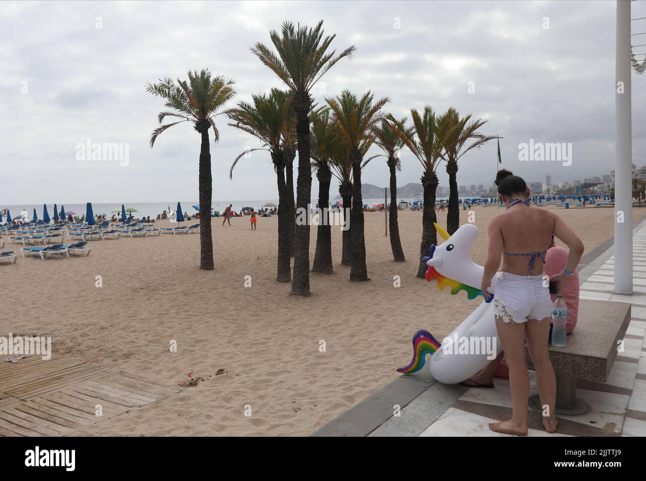 Benidorm, Spain. 27th July, 2022. Holidaymakers carry an inflatable unicorn at the beachfront in Benidorm, Spain. Credit: Isabel Infantes/Alamy Stock Photo