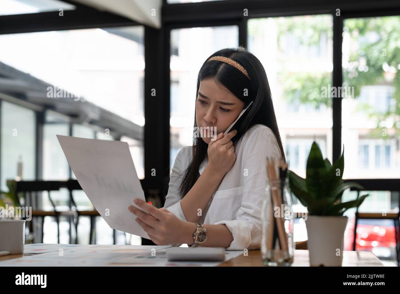 Business asian woman working with paperwork calculator at office while talking on phone, Stock Photo