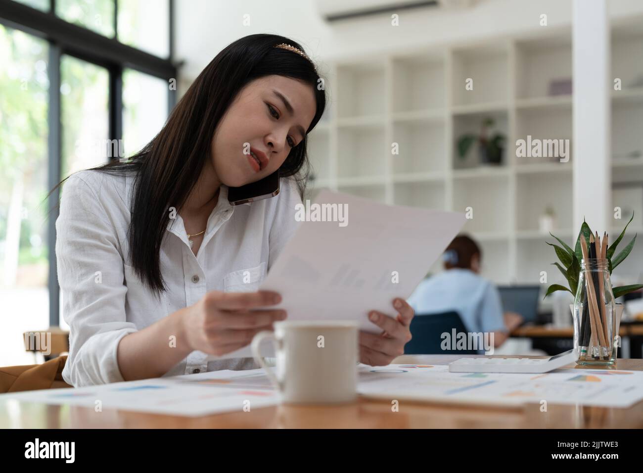 Business asian woman working with paperwork calculator at office while talking on phone, Stock Photo