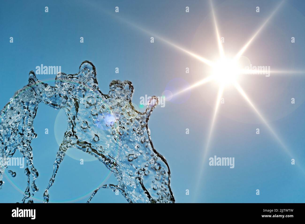 Jet of water in front of blue sky with sun Stock Photo