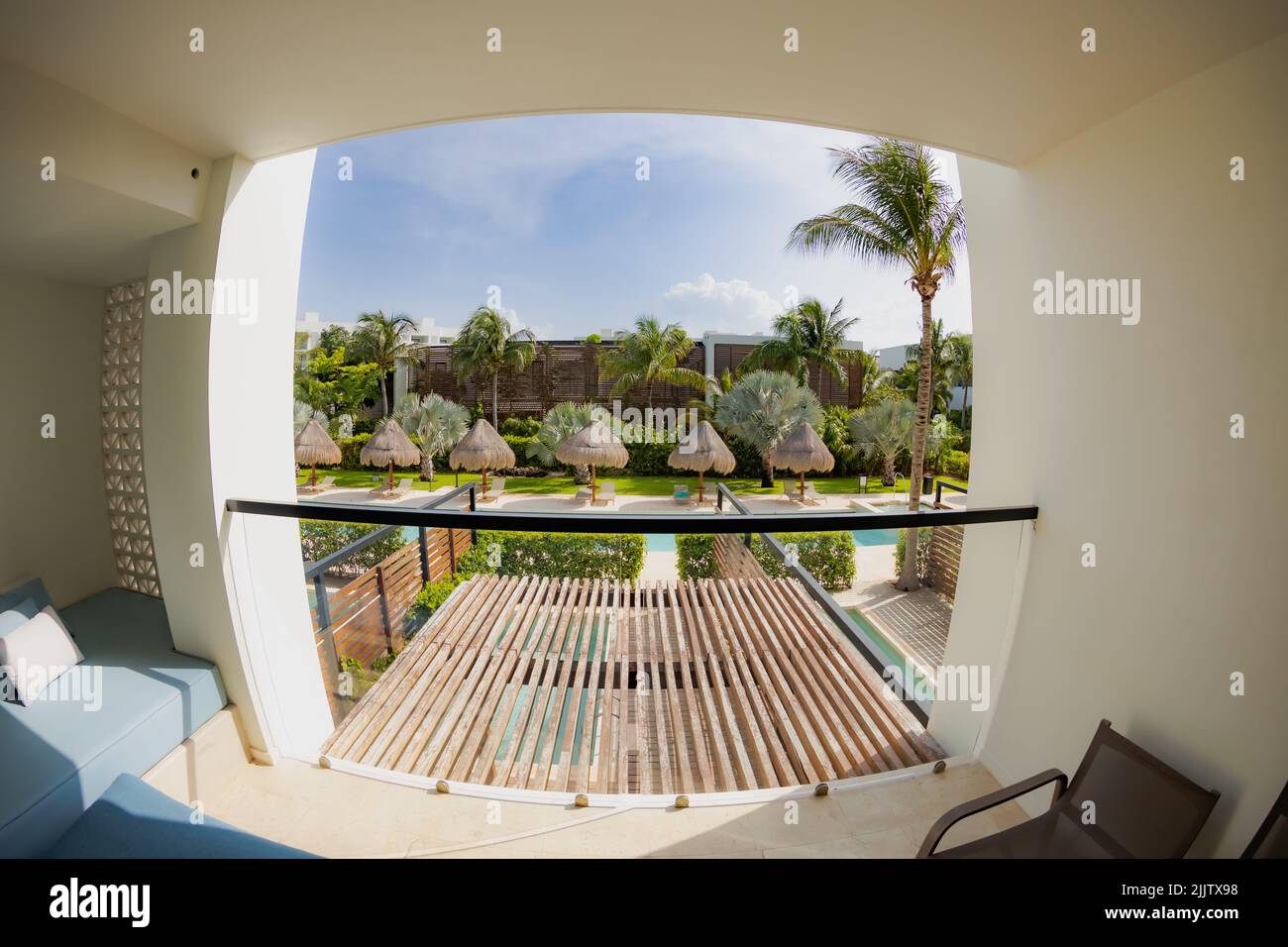 A view of a terrace with a pool, palms, and umbrellas from the hotel room balcony shot with a fish eye lens Stock Photo