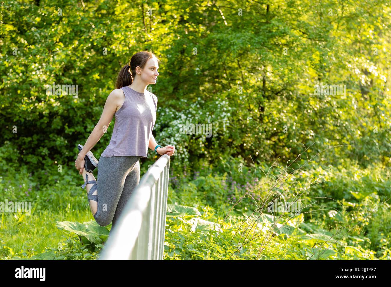 A young Caucasian female doing stretching exercises by the railing in a ...