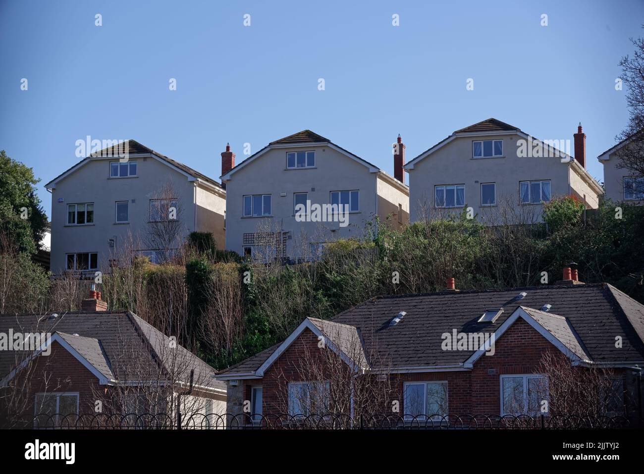 Row of identical detached houses built on the hill overlooking a residential area. Stock Photo