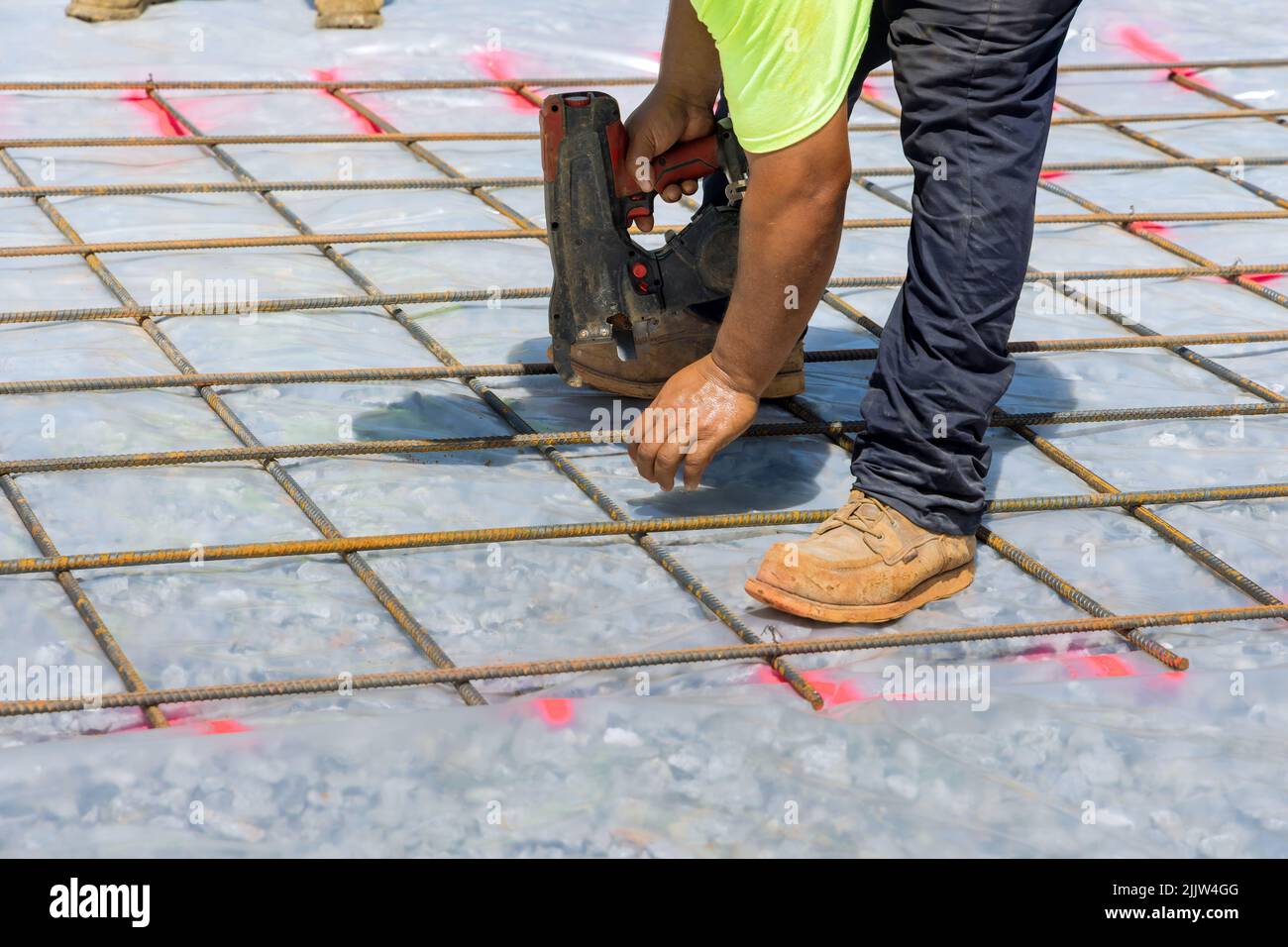 Construction worker twist steel bars with wire rod reinforcement into cement foundations using a tool known as the rebar tying tool. Stock Photo