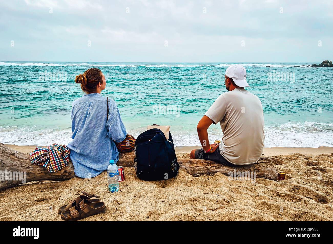 A back view of two friends sitting on the beach and looking at the ocean in Santa Marta, Colombia Stock Photo