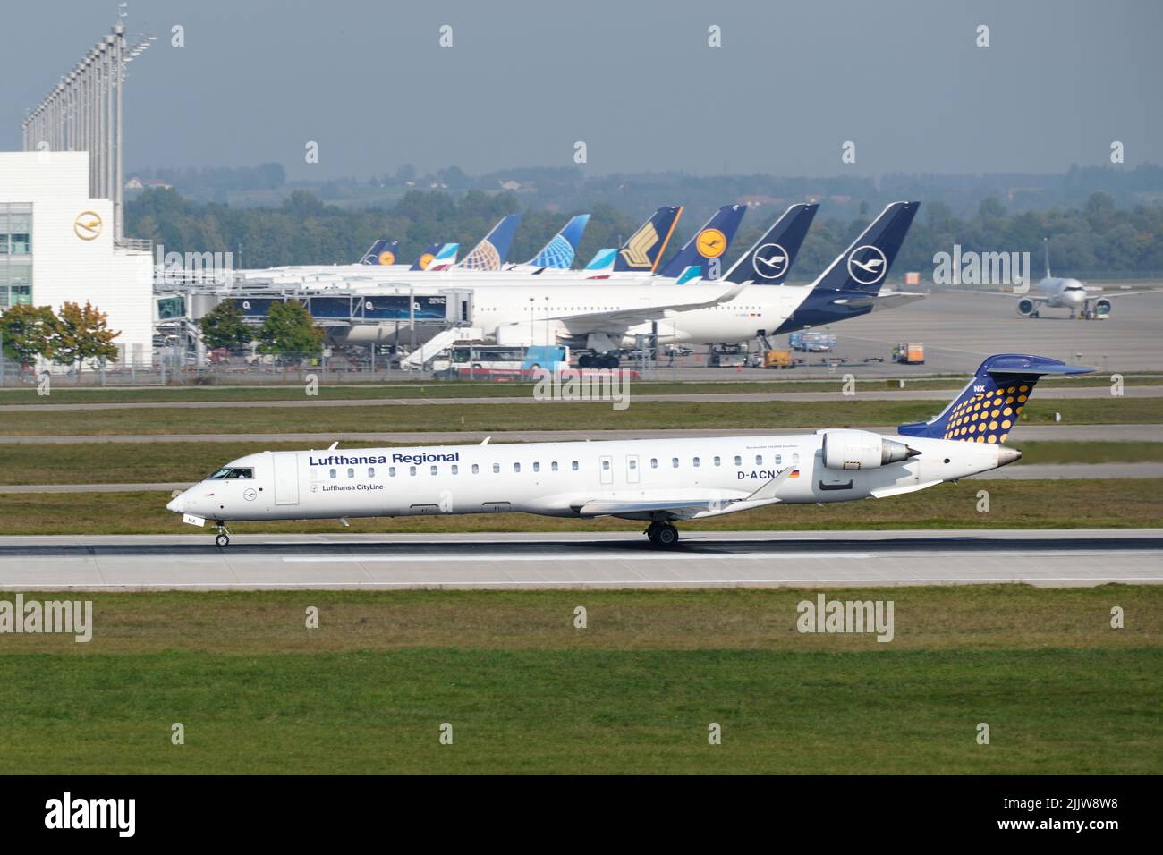 Departing Lufthansa Regional jet in front of parked aircraft at the terminal of Munich Airport, Germany, local transportation with short-haul flights. Stock Photo
