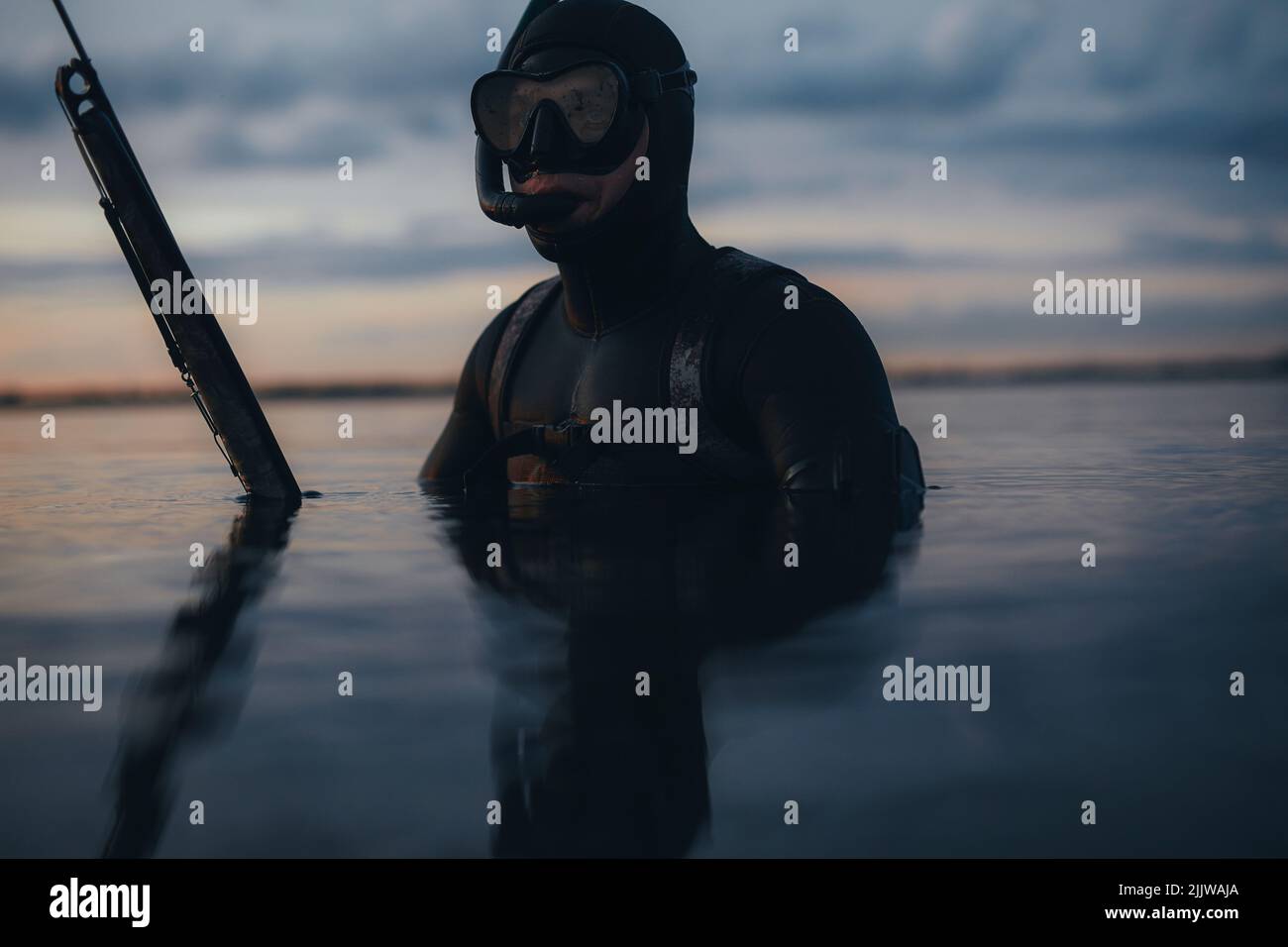 Man in a wetsuit and a scuba mask holding a speargun. Male diver spearfishing in the middle of the ocean. Stock Photo