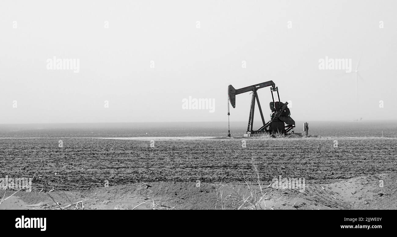 Oil rig pump jack in an arid oil field of west Texas with a wind