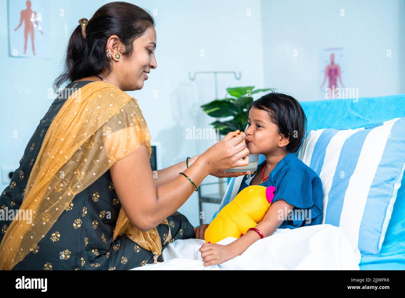 Mother feeding porridge to ill kid while admitted at hospital ward - concept of parental caring, medical treatment and health care. Stock Photo