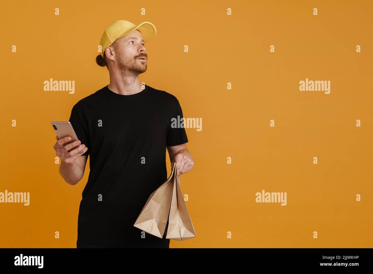White delivery man with paper bags using mobile phone isolated over yellow background Stock Photo