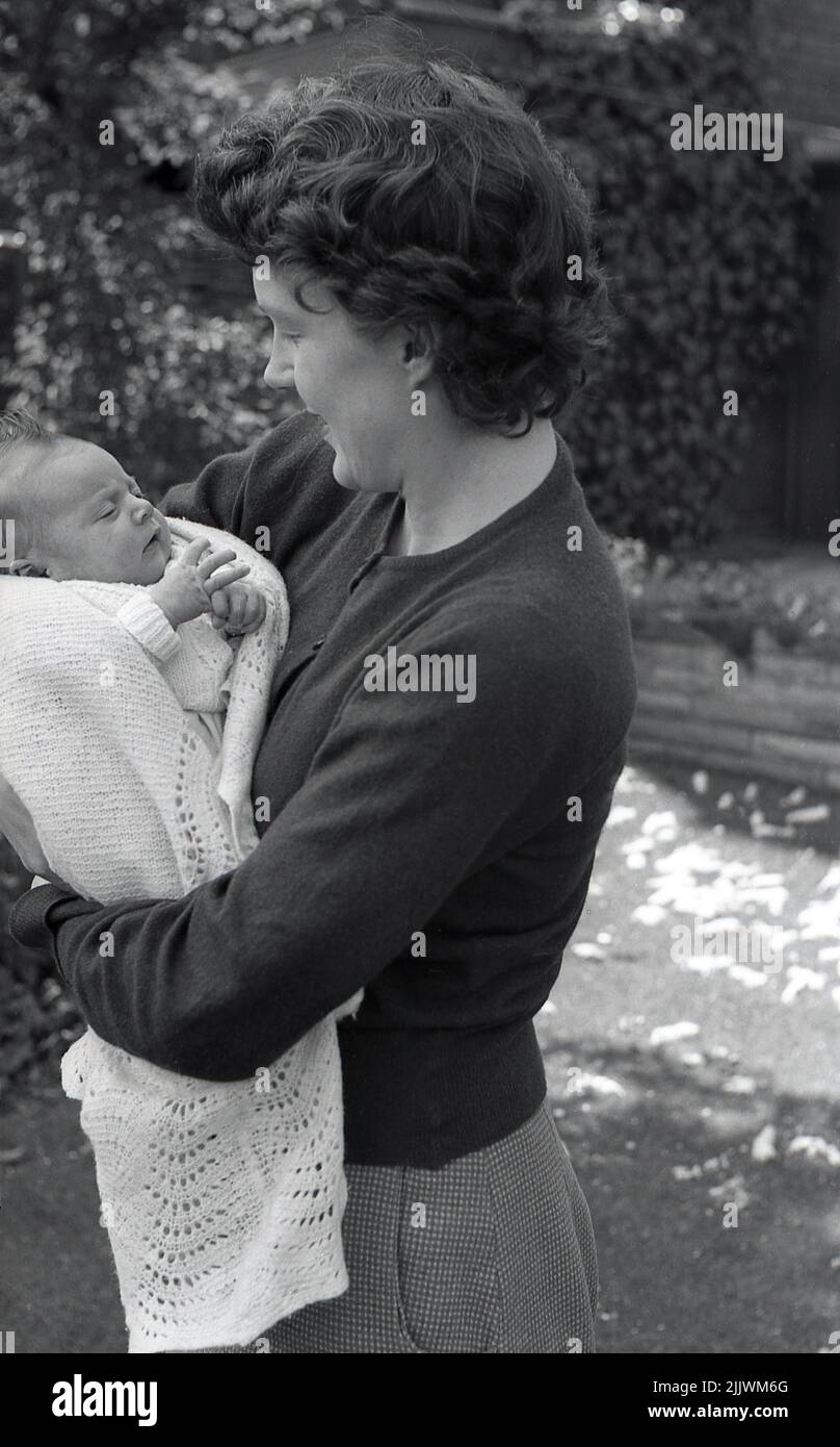 1960s, historical, outside, a mother holding closely her newly born baby, wrapped in a cotton shawl, in her arms, England, UK. Stock Photo