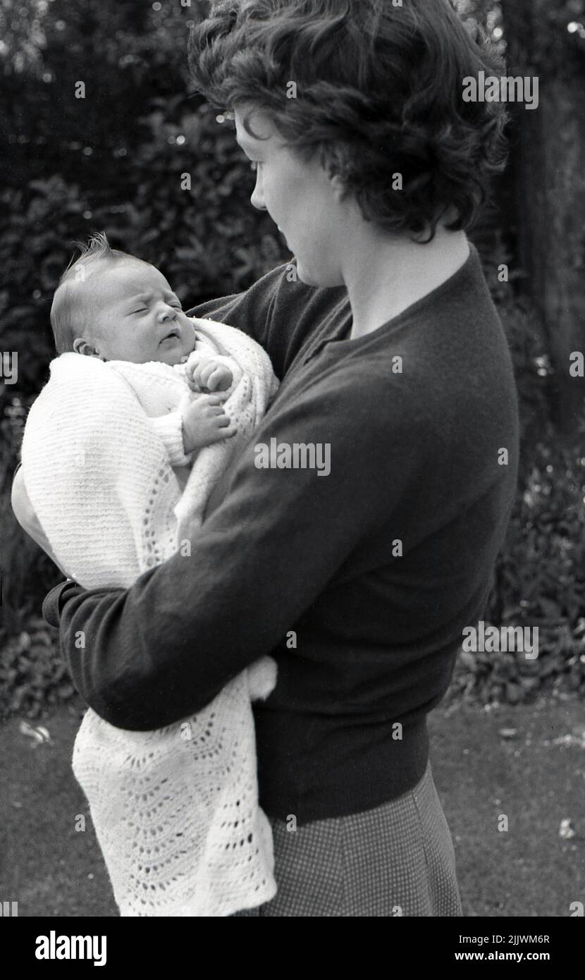 1960s, historical, outside, a mother holding closely her newly born baby, wrapped in a cotton shawl, in her arms, England, UK. Stock Photo