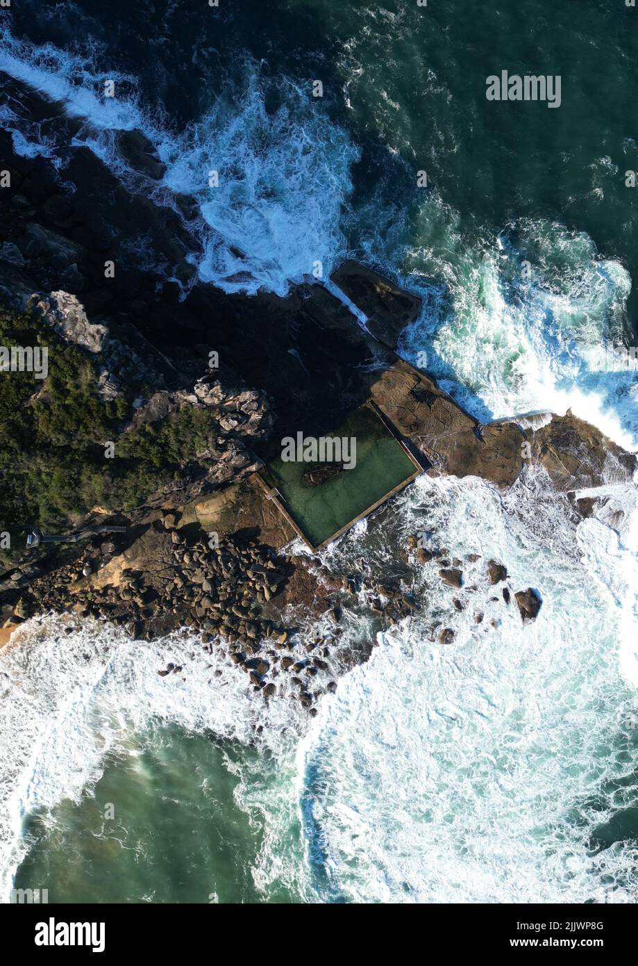 A vertical aerial view of a blue wavy ocean and a cliffy shore during a ...