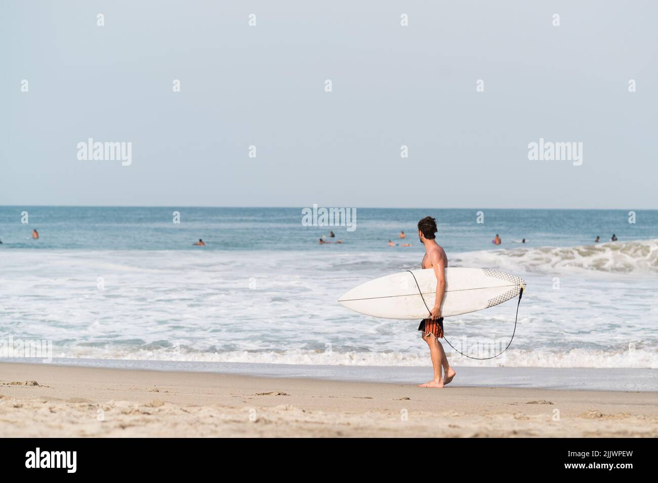 A surfer man holding surfboard and walking on the beach in Puerto