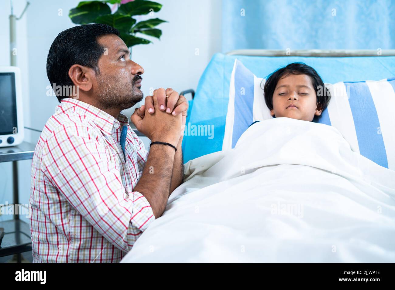 Worried father praying for sick girl child recovery near bed at hospital ward - concept of medical treatment, hope and family bonding Stock Photo