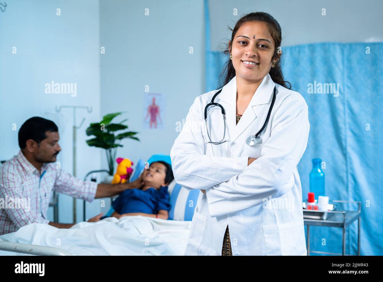 Happy confident doctor with arms crossed standing in front of patient by looking at camera at hospital - concept of medical treatment, professional Stock Photo