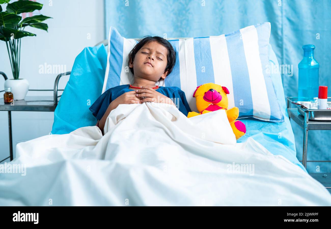 Sick girl child with teddy bear sleeping on bed at hospital - concept of medial treatment, illness and childcare. Stock Photo