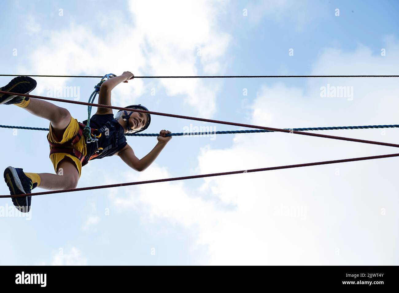 Child in safety harness and helmet in rope park. Boy climbs attached ...