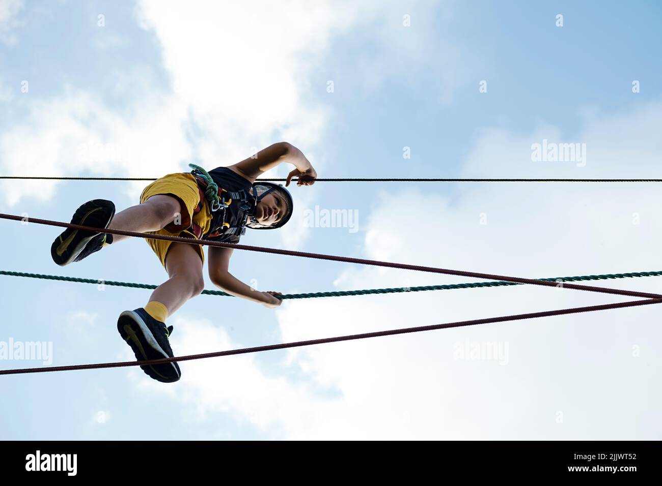 Child in safety harness and helmet in rope park. Boy climbs attached ...