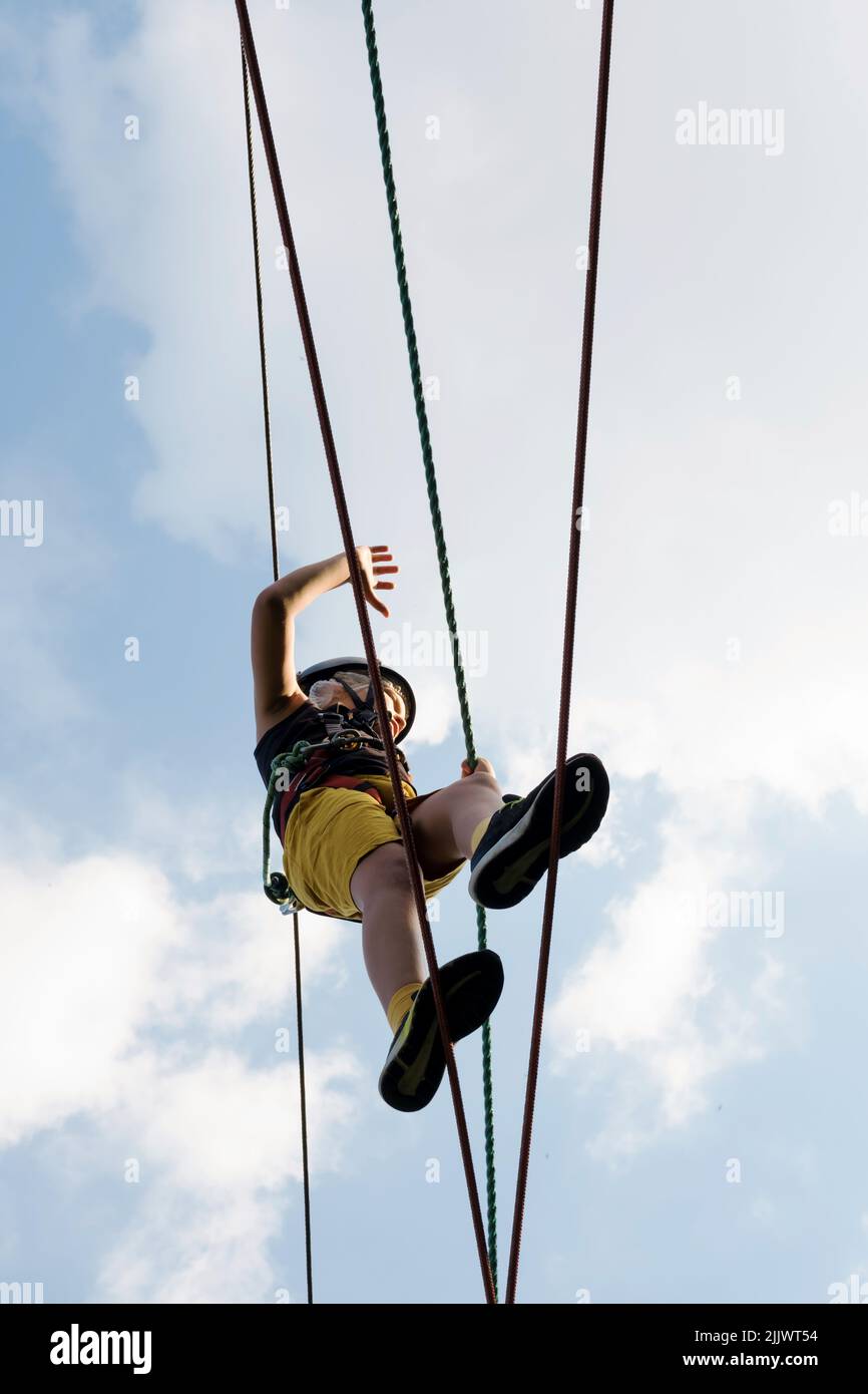 Child in safety harness and helmet in rope park. Boy climbs attached ...