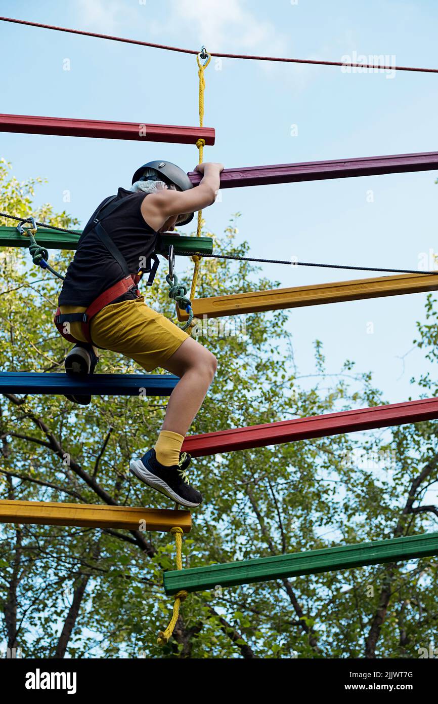 Child in safety harness and helmet in rope park. Boy climbs attached ...