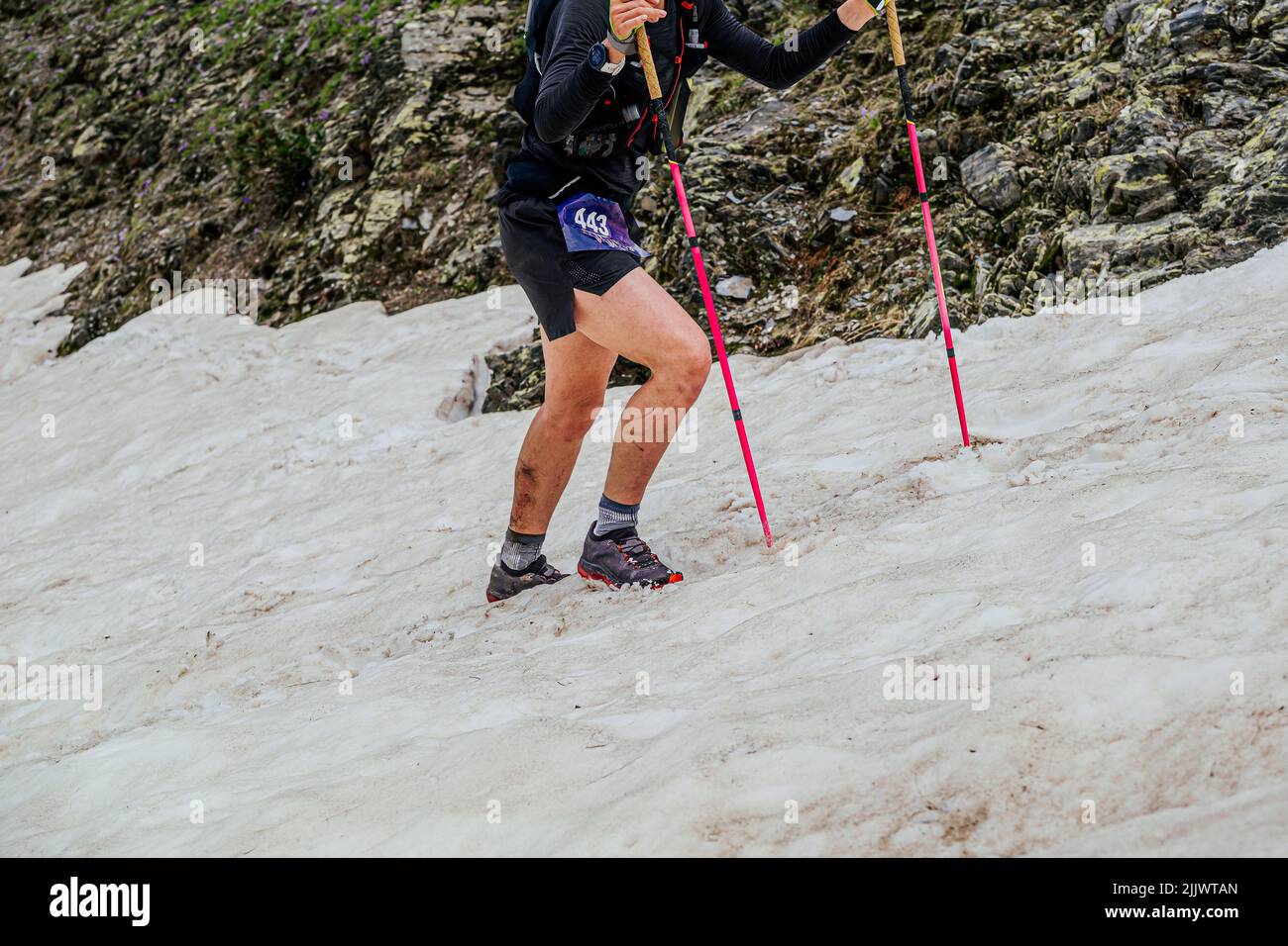 female athlete climbing uphill in snow with trekking poles Stock Photo