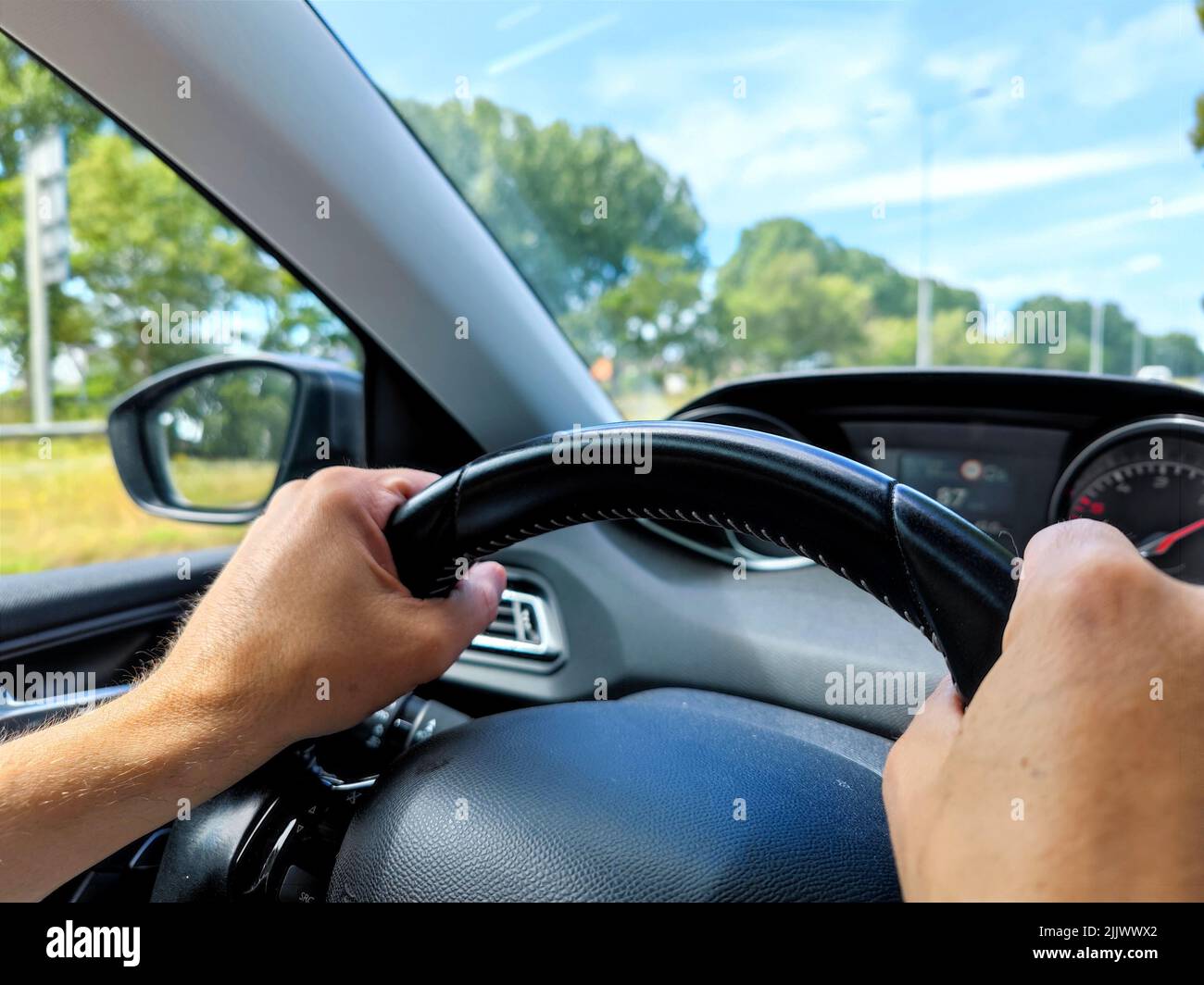 White men hands control a car steering wheel while driving on the road. There are no recognizable persons or trademarks in the shot. Stock Photo