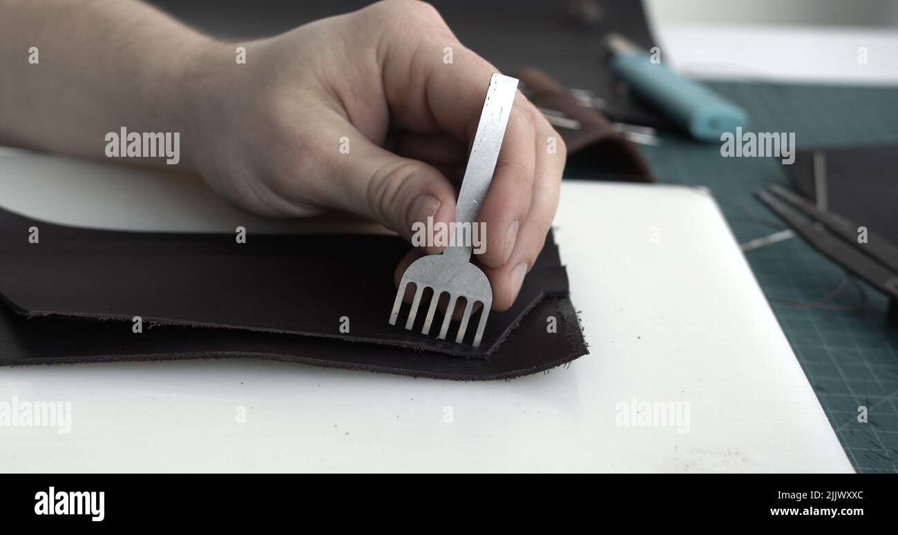 Close up men's hands make a leather product. Punching holes in the