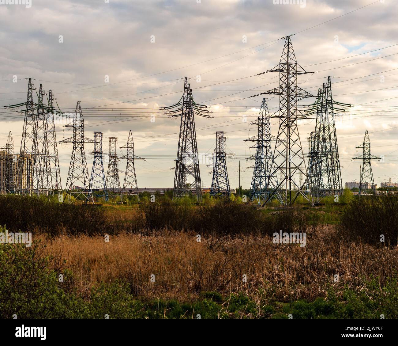 A view of power lines in a green field under a cloudy sky Stock Photo