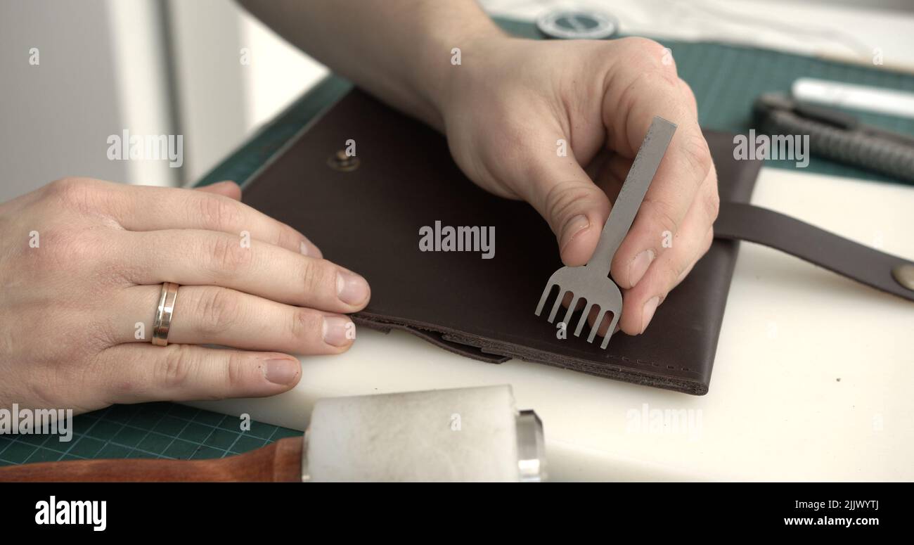 Craftsman making holes in leather with puncher tool. Working process