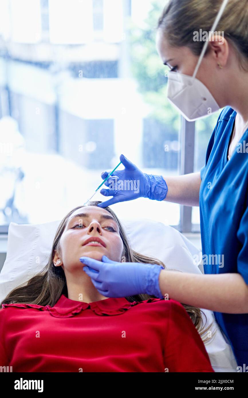 Esthetician in uniform and face mask injecting collagen into forehead ...