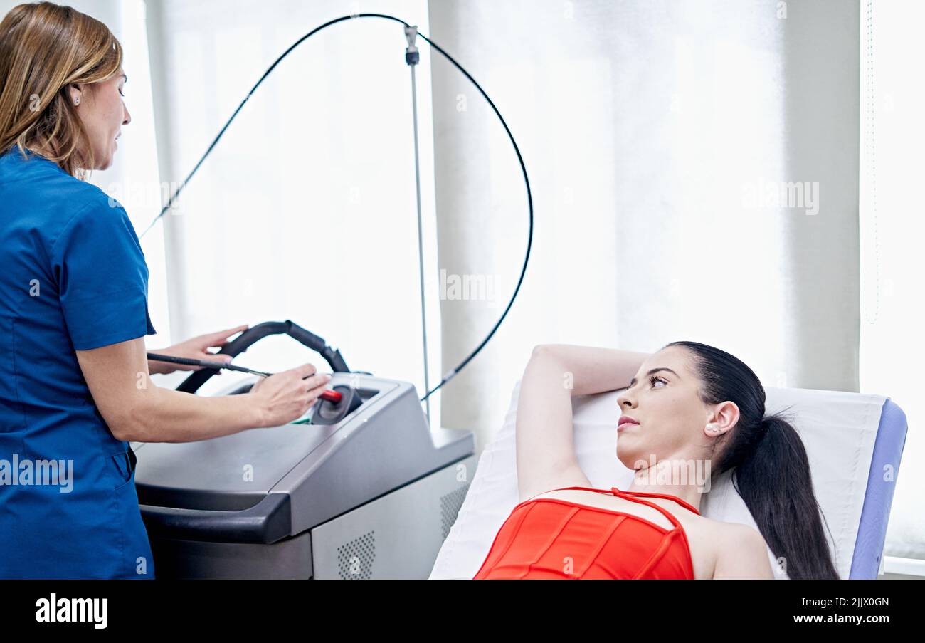 Female esthetician preparing machine for laser epilation near Woman
