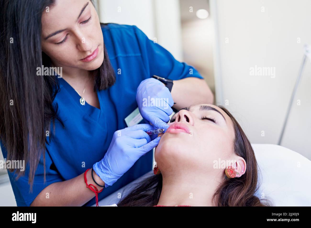 From above esthetician in latex gloves injecting collagen into lips of ...