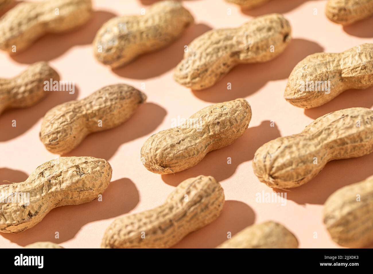 From above fresh peanuts in shells forming seamless pattern on peach background Stock Photo