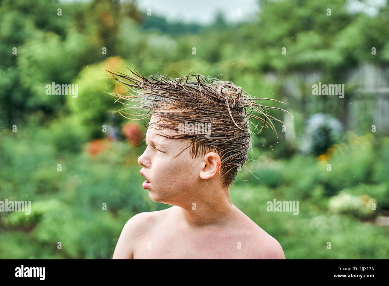 Cute blond boy twists wet head in different directions on blurred background. Schoolboy with funny facial expression after swimming in pool closeup Stock Photo