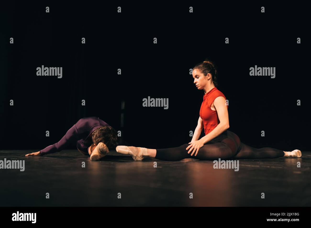 Full body male and female ballet dancers doing splits and stretching on dark stage during rehearsal in theater Stock Photo