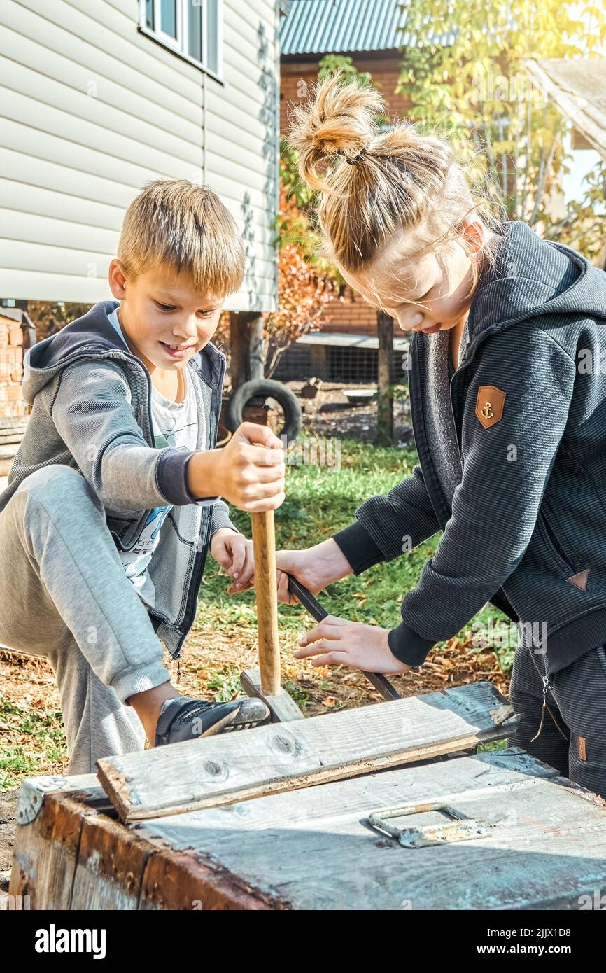Brothers help grandpa in village to dismantle old beehives on sunny day. Cute boys with blond hair enjoys household in backyard near house Stock Photo