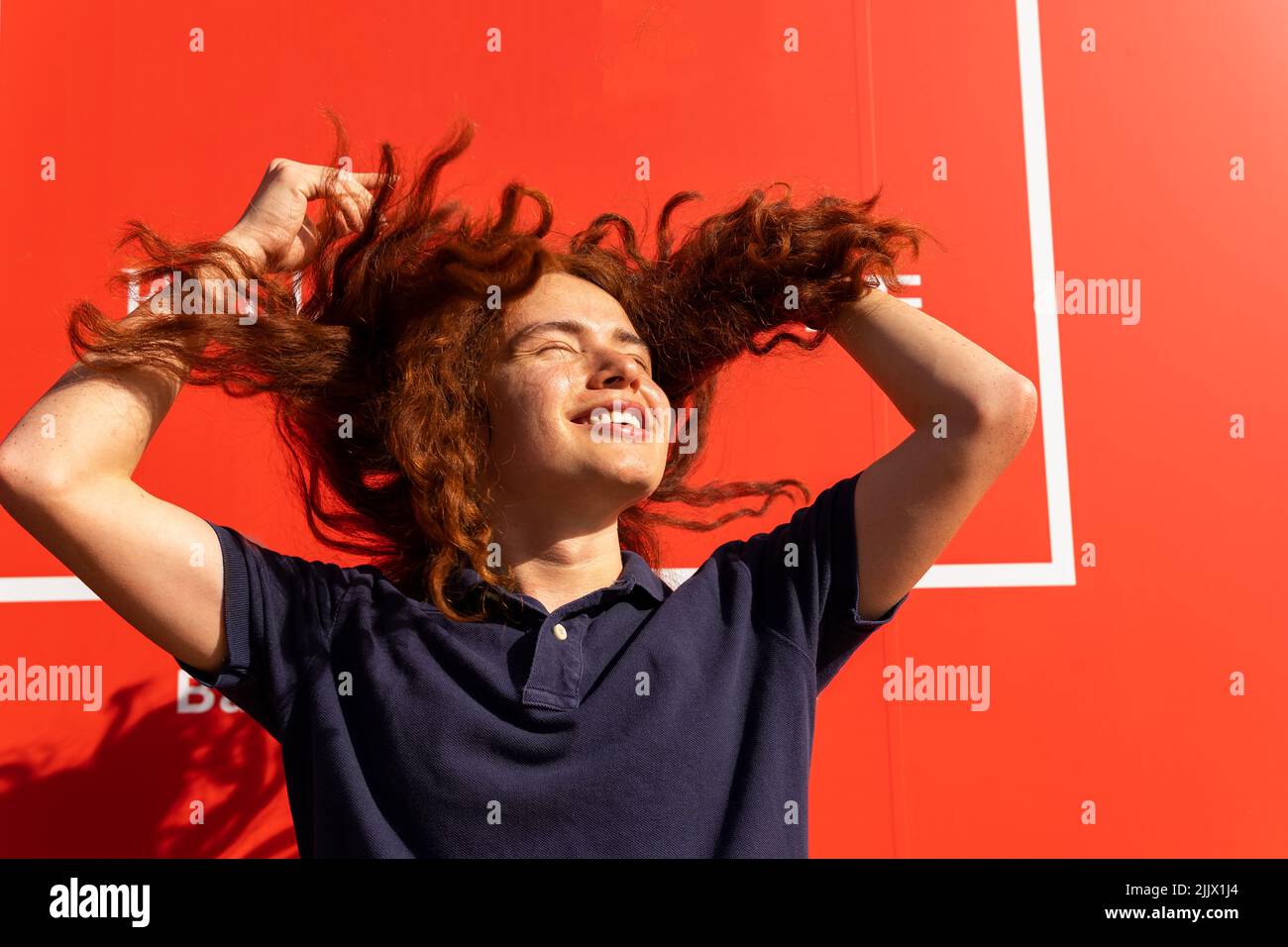 Cheerful young Woman with tousled brown hair standing against wall Stock Photo