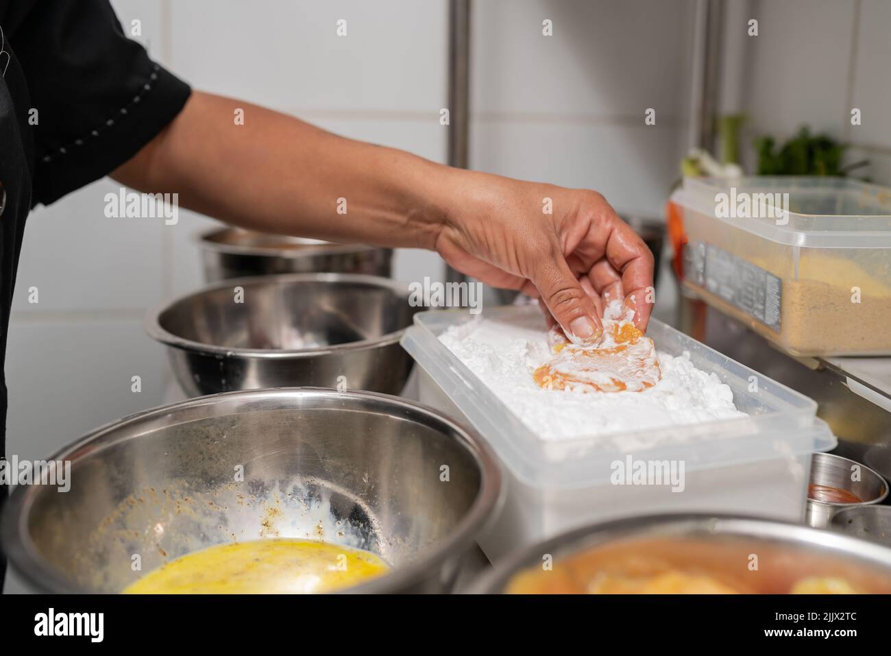 Crop anonymous chef coating raw chicken wing with flour in container at