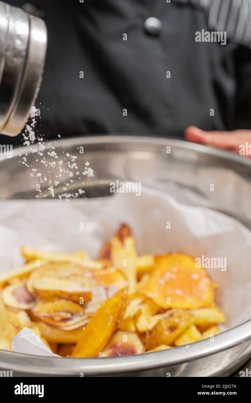 Crop anonymous chef in black uniform sprinkling salt into glass bowl ...