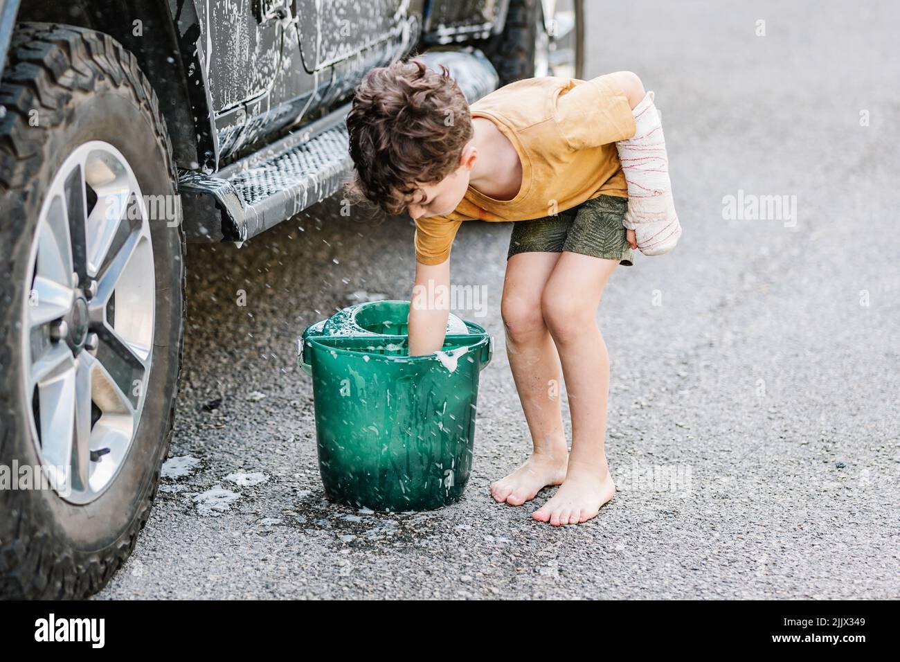 Full body of Caucasian boy putting hand in bucket while washing car
